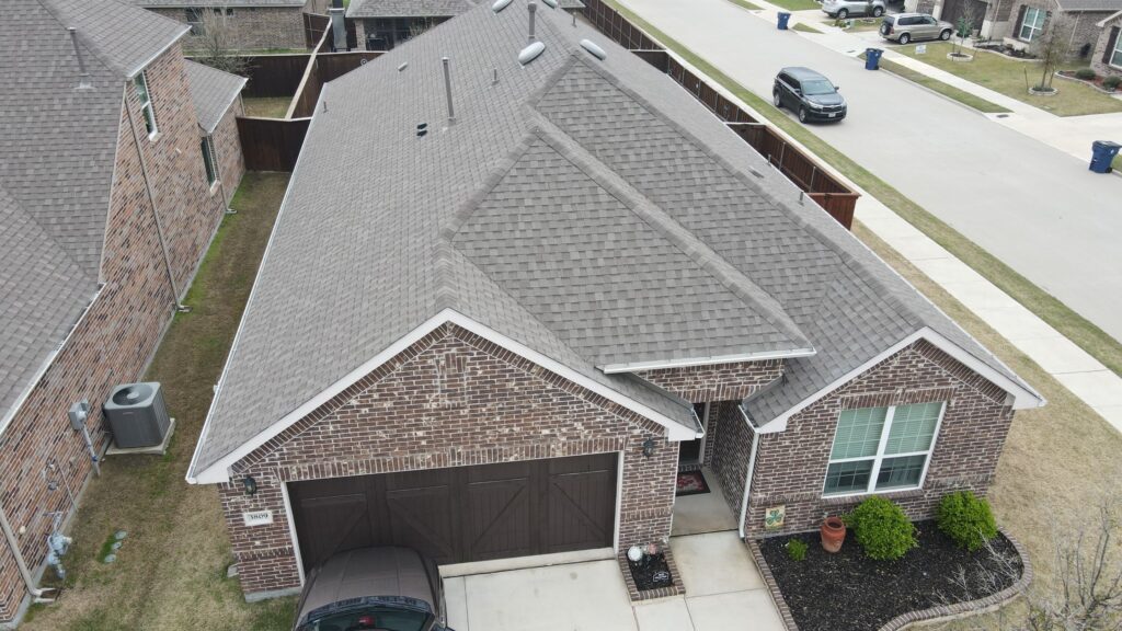 Aerial view of a completed architectural-shingle hip roof on a brick Celina, Texas home