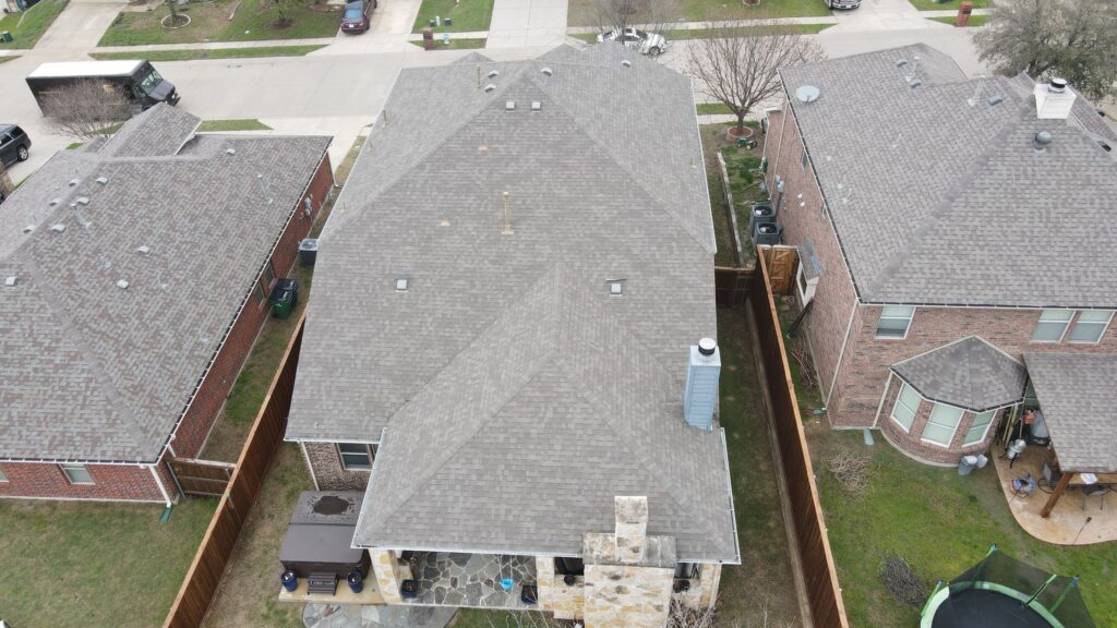 Aerial view of a gray architectural-shingle hip roof over a brick home with a fenced backyard in Celina, Texas