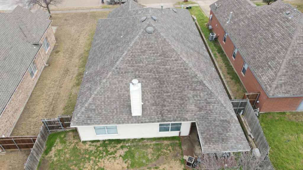 Aerial view of a gray architectural-shingle hip roof over a light-sided home with a fenced backyard in Celina, Texas