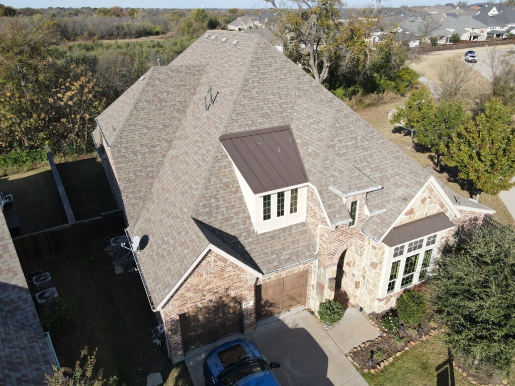 Aerial view of a completed hip-and-gable architectural shingle roof on a brick and stone Allen, Texas home