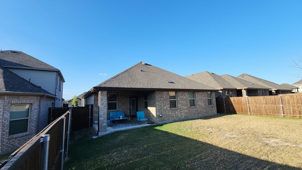Rear view of a brick home with a brown architectural-shingle hip roof and a fenced backyard in Celina, Texas