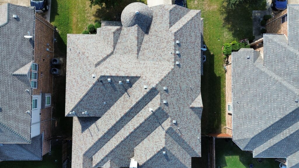Aerial view of a light architectural-shingle hip roof with a rounded turret on a neighborhood home in Celina, Texas