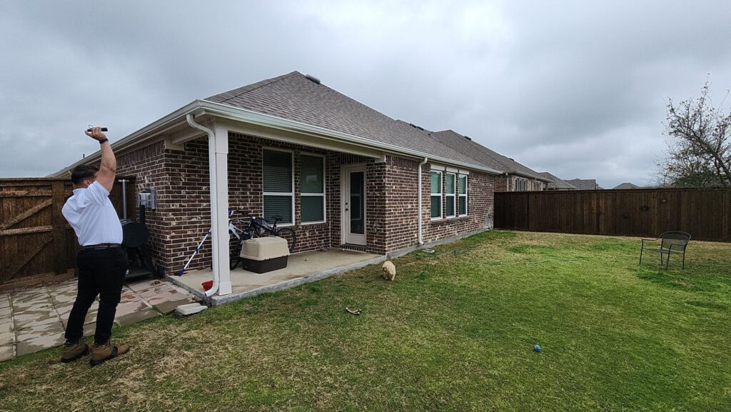 Rear view of a brick home with a brown architectural-shingle hip roof and a covered patio in Celina, Texas
