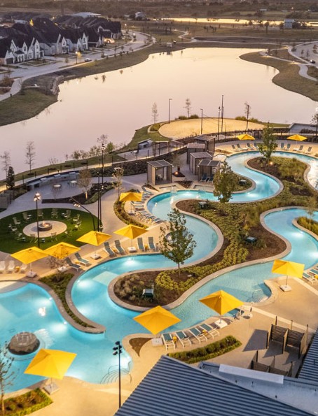 Aerial dusk view of Mosaic’s winding lazy river, yellow umbrellas, and lake in Celina, Texas