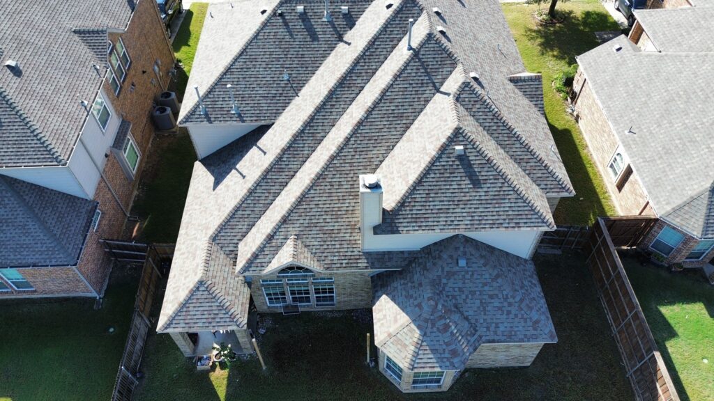 Overhead view of a multi-plane gray architectural-shingle hip roof with a chimney and bay in a Celina, Texas neighborhood
