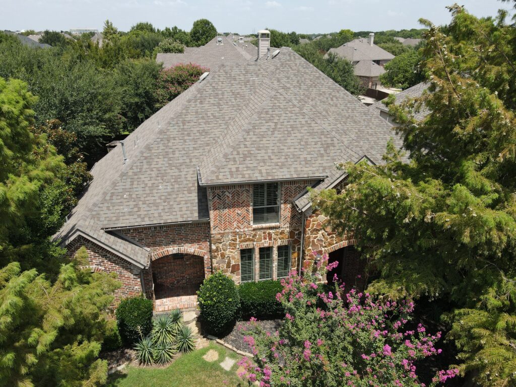 Aerial view of a completed hip-and-gable architectural shingle roof on a brick and stone Allen, Texas home