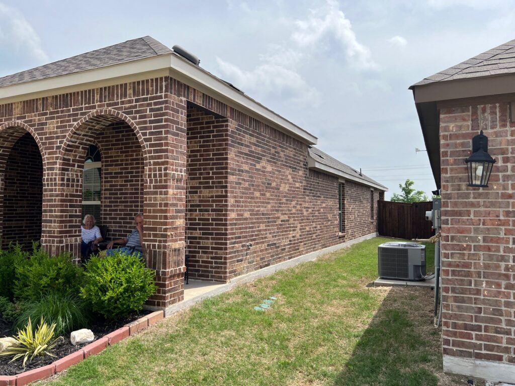Side view of a brick home with a brown hip roof, arched porch, and covered patio in Celina, Texas