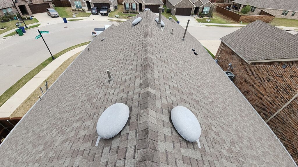Aerial view down a gray architectural-shingle hip-roof ridge with two mushroom vents in a Celina, Texas neighborhood