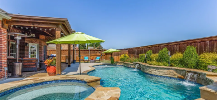 Backyard gunite pool and raised spa with a lime patio umbrella and covered outdoor kitchen in Allen, Texas