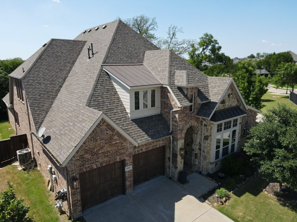 Aerial view of a completed tan architectural-shingle hip roof on a brick and stone two-story Allen, Texas home