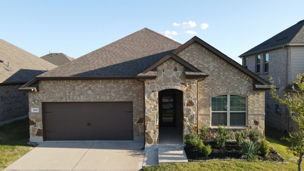 Tan brick ranch home with a stone-arch entry, brown garage door, and gray architectural-shingle hip roof in a Celina, Texas neighborhood