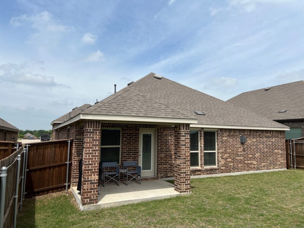 Red brick ranch with a gray architectural-shingle hip roof, rear patio, and two folding chairs in a Celina, Texas neighborhood