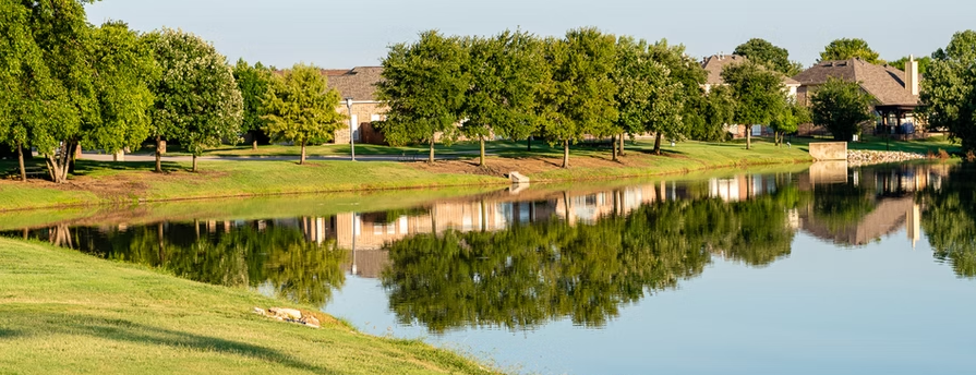 Pond reflecting trees and rooftops in The Trails of West Frisco, Texas