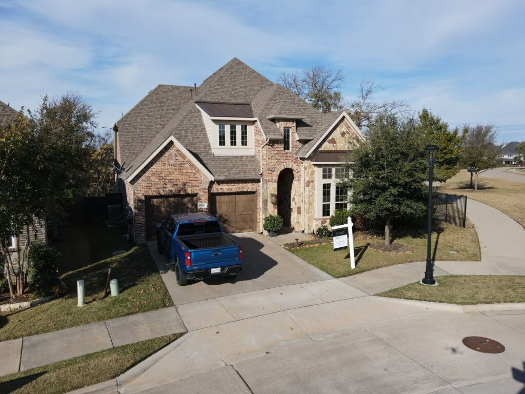 Aerial view of a completed brown architectural-shingle hip roof on a brick and stone Allen, Texas home