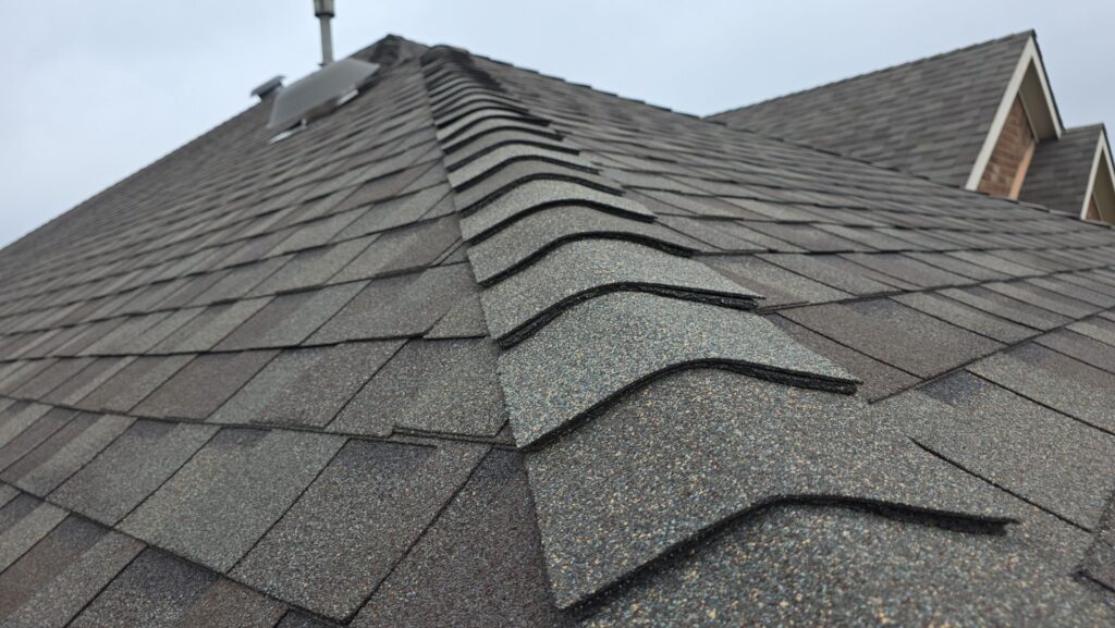 Close-up of gray architectural ridge-cap shingles running up a hip roof in a Celina, Texas neighborhood