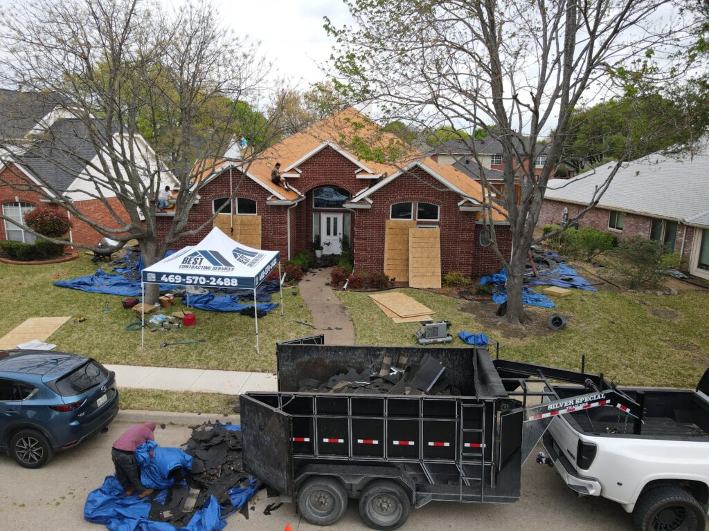 Best Contracting crew tearing off shingles on a brick ranch roof with dumpster and tent in Allen, Texas