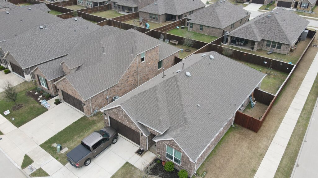 Aerial view of neighboring brick ranch homes with gray architectural-shingle hip roofs and a pickup in the driveway in Celina, Texas