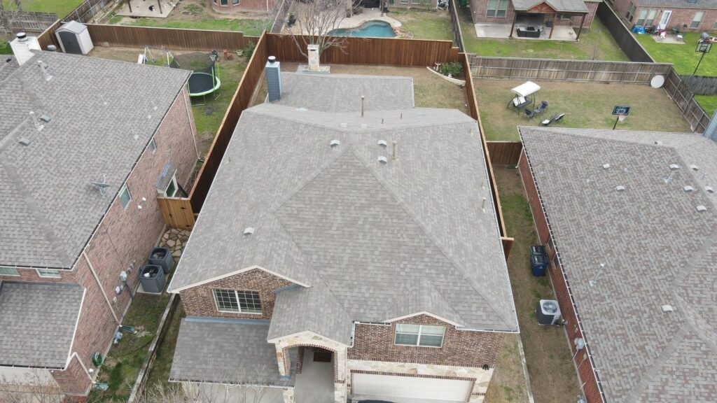 Overhead view of a two-story brick home with a gray architectural-shingle hip roof and a white garage door in a Celina, Texas neighborhood